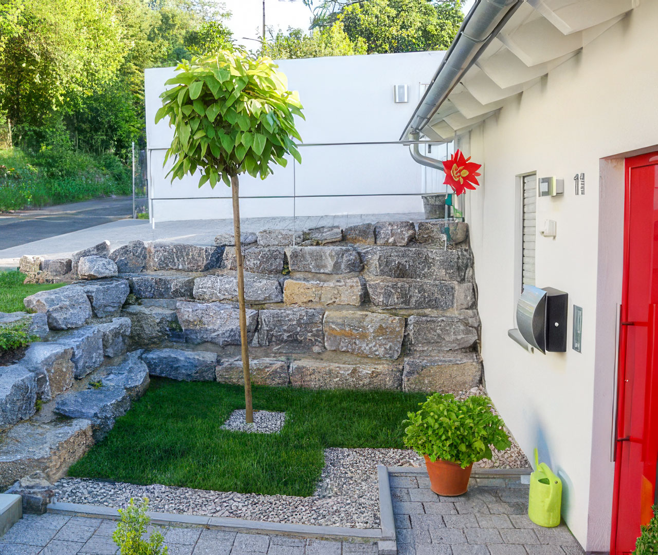 Individuell gestalteter Vorgarten mit Natursteinmauer und roter Haustür